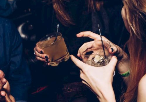People enjoying drinks at a social gathering, holding cocktails and chatting in a lively atmosphere.