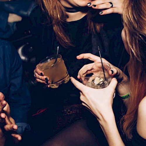 People enjoying drinks at a social gathering, holding cocktails and chatting in a lively atmosphere.