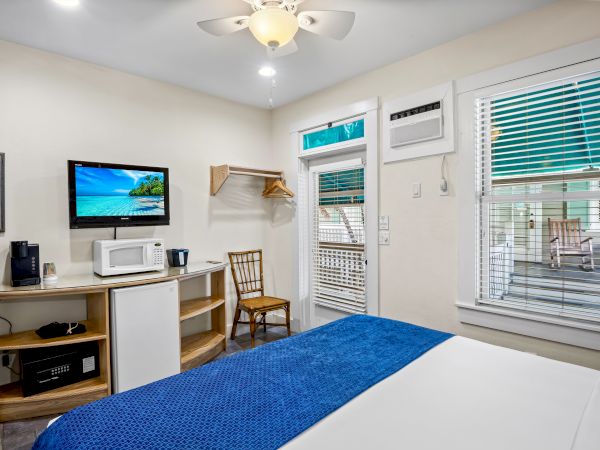 A cozy room with a bed, TV, microwave, and coffee maker. It has a window, chair, ceiling fan, and open closet space.