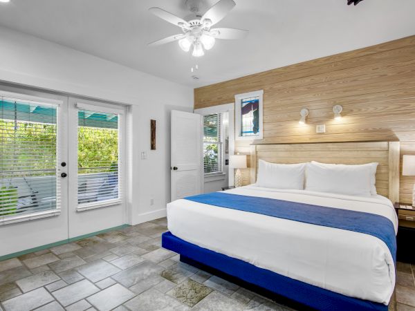 A modern bedroom with a king-sized bed, blue accents, wood paneling, two lamps, a ceiling fan, and glass doors leading outside.