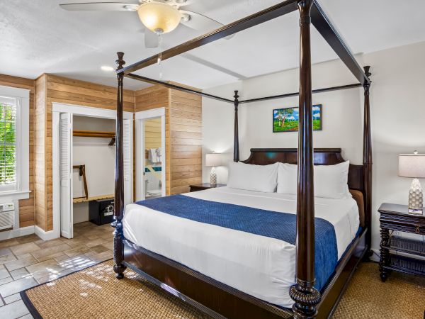 The image shows a bedroom with a four-poster bed, blue accent, nightstands, a lamp, open closet, tiled floor, and a ceiling fan.