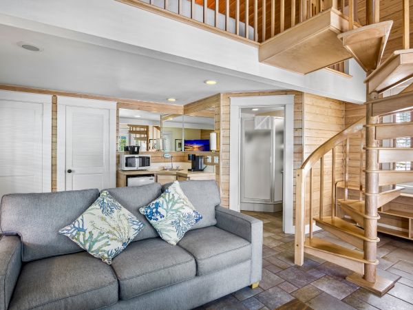 A cozy room featuring a spiral staircase, a gray sofa with patterned pillows, and a compact kitchen area in a modern, wooden interior design.