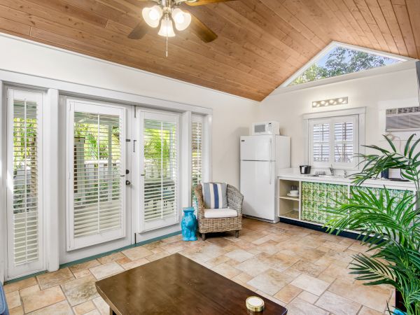 Cozy room with French doors, tiled floor, wooden ceiling, kitchenette, and a plant for decor. Natural light streams in beautifully.