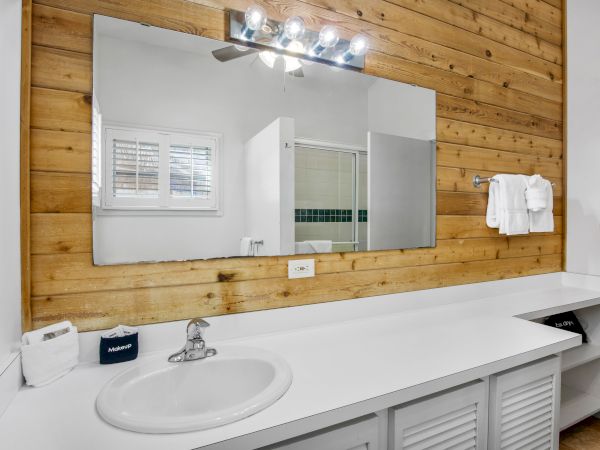 A bathroom with a white countertop, a sink, a large mirror, wood paneling, and a towel rack with white towels.