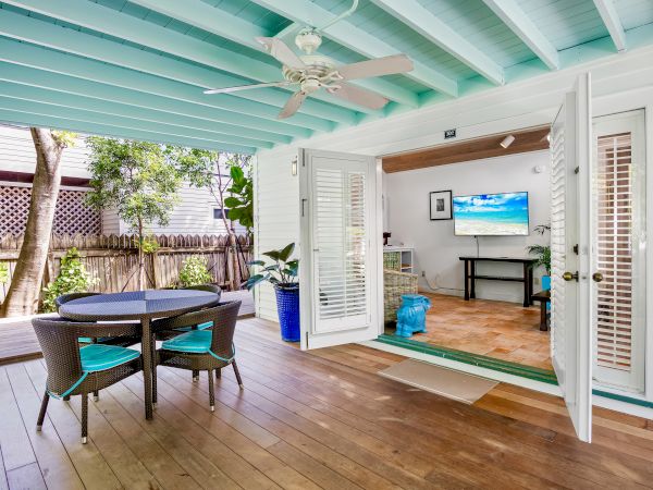 A cozy patio with a round table and chairs, leading into a living room with open doors and a TV on the wall.