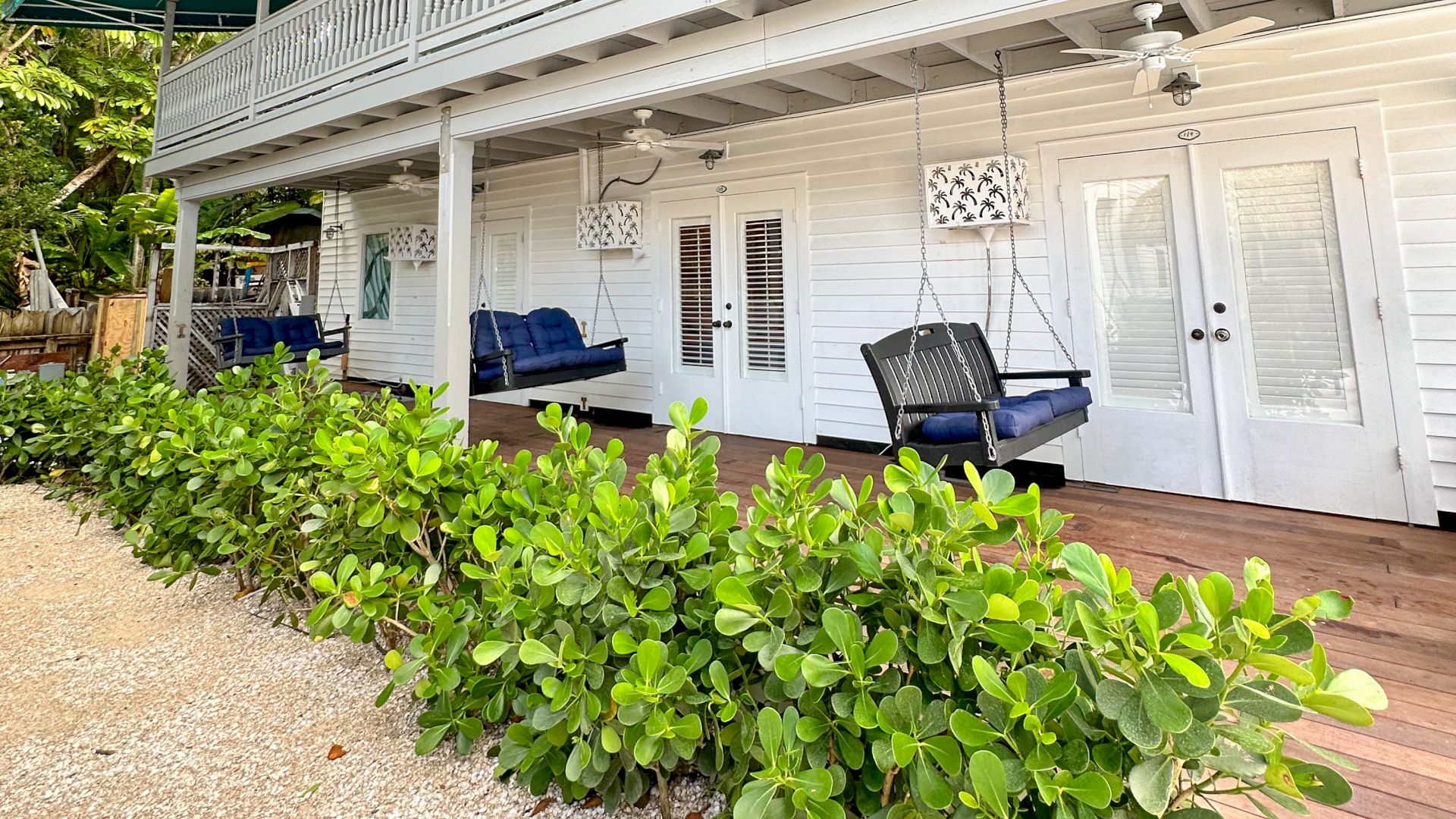 A white two-story house with green awnings, a large porch, swings, and plants in the foreground.