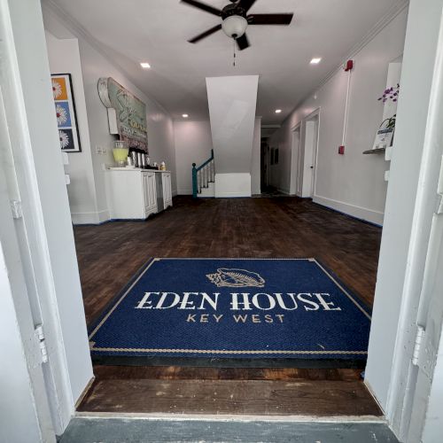 An entryway with a mat reading "Eden House Key West," leading into a well-lit interior space with wooden flooring and a ceiling fan.